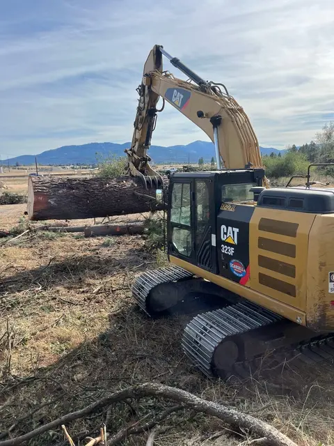 Excavator with grapple stacking sawlogs on a log deck during a small-tract harvest